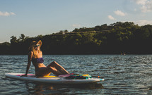 woman in a bikini sitting on a surfboard 
