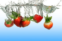 Strawberries submerged into water creating a splash.