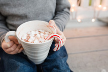 child holding a mug of hot cocoa with a candy cane 