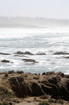 Ocean waves crashing onto rocks on a hazy day.