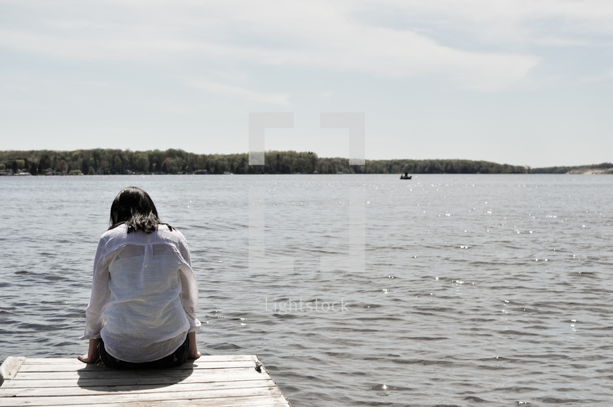a woman sitting at the end of a dock 
