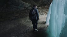 a man walking in a cave looking at a frozen waterfall 