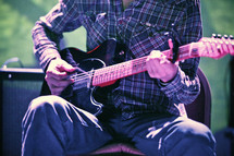 musician sitting and playing an electric guitar