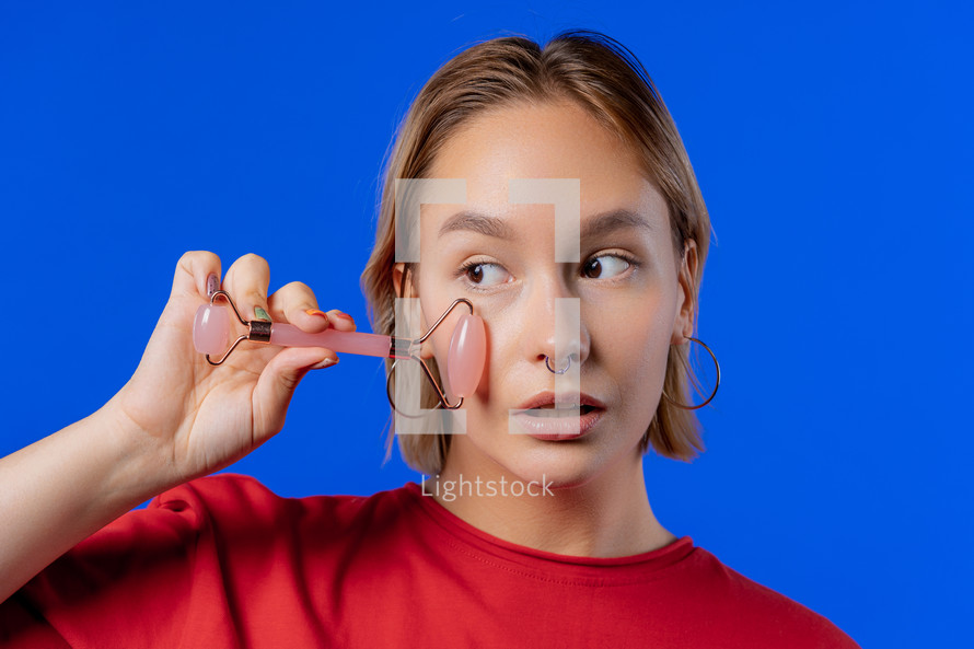 Teen girl with rose quartz stone roller on blue background