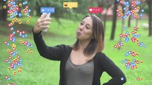 Girl taking selfies with animated social media emojis on either side of her.