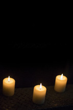 Three white votive candles with flame.