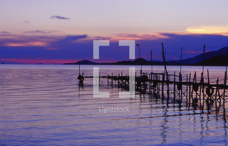 a rustic pier over water at sunset 