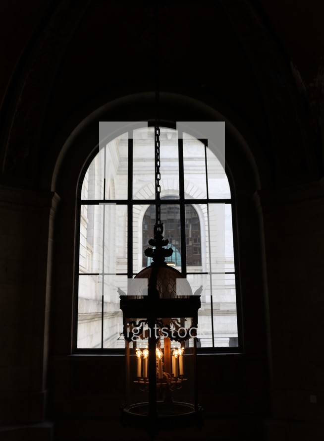 lamp hanging from a ceiling in front of a window in a cathedral 