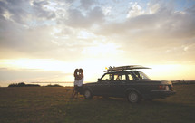 couple kissing leaning against a car with surf boards on top