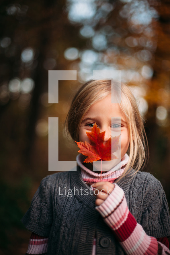 a girl holding a fall leaf in front of her face 