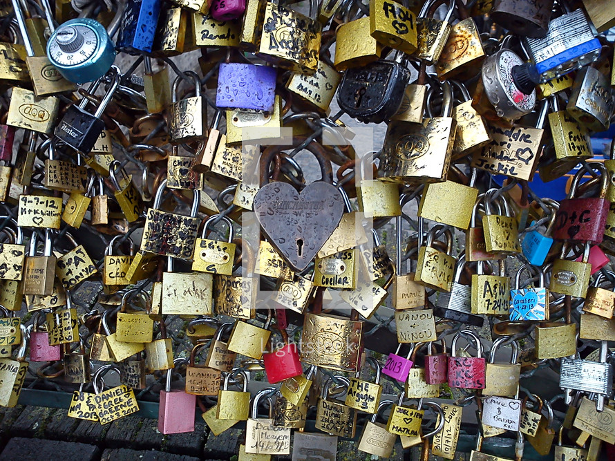 Padlocks with names written on them attached to and covering a fence.