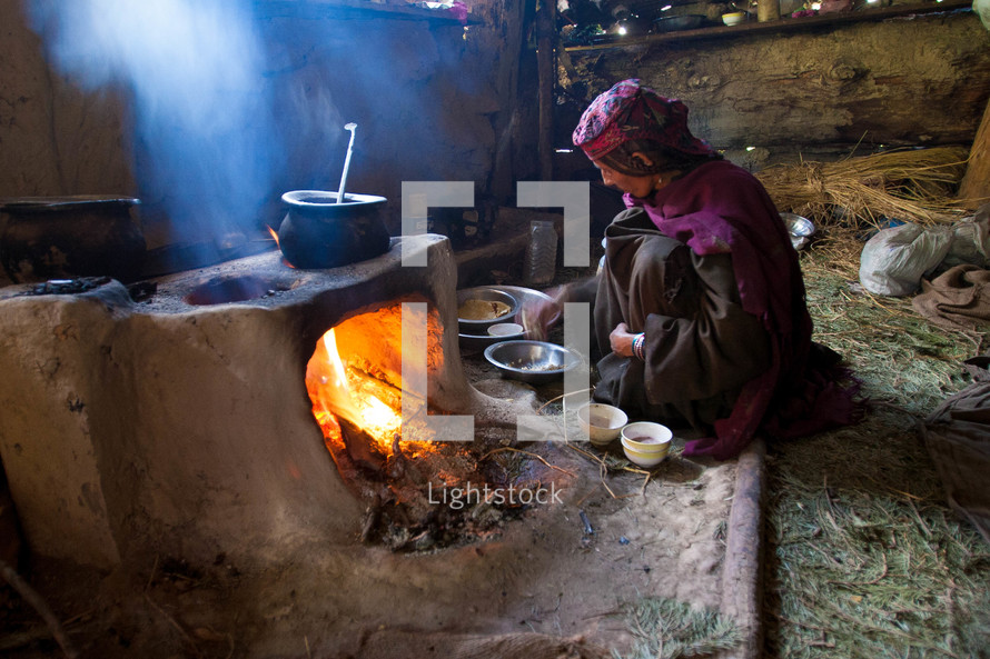 A woman cooking at a clay stove in a hut 