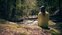 a woman sitting outdoors listening to water flow in a stream 