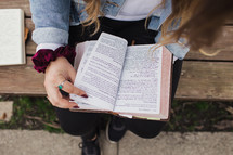 a young woman sitting on a bench reading a Bible 
