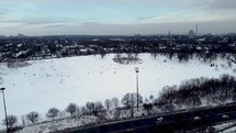 Aerial shot of Riverdale Park East in dynamic cityscape in Toronto on a winter day. Drone flying over Don Valley Parkway. View people sliding on the snow while aircraft does an orbit movement.