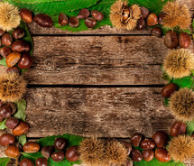 Frame of chestnuts, leaves and chestnut bur on wooden table