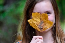 a girl hiding behind a fall leaf 