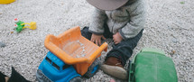 toddler boy playing in gravel with a toy dump truck 