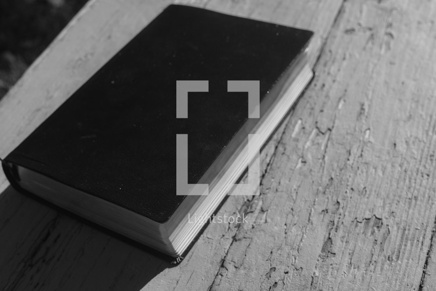 A Bible laying closed on a rustic wood surface.