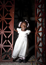 Smiling girl in white dress emerging from doorway.