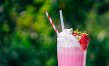 Still life - creamy strawberry milkshake cocktail or smoothie with straw on nature backdrop. Appetizing summer dessert. Healthy berry food. High quality 