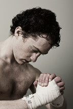 Sweaty man with hands wrapped in fighter's style, hands clasped in prayer.