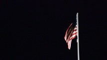 spotlighted American flag on a flagpole at night at the roof of the American embassy