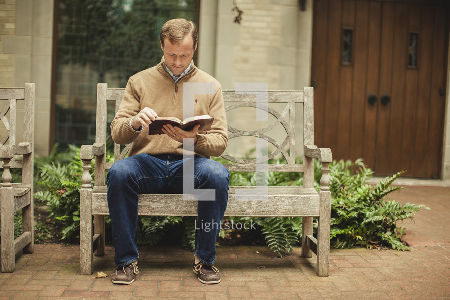 Man on bench reading Bible