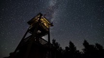 Time lapse of Milky way galaxy and stars over lookout tower in starry night sky.