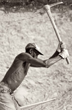 A man working in a field swinging a pick ax