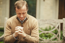man with head bowed in prayer with fingers laced