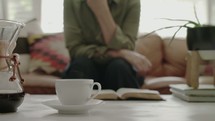 a cup of steaming coffee and a woman sitting on a couch 