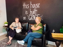 Two women chatting in front of "This house is built on Grace" mural