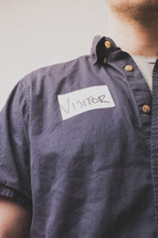 Man in a denim shirt with a visitor's tag.