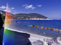view of the ocean from a shore with rainbow sun flare 