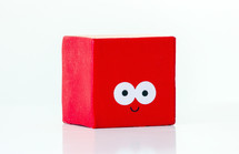 Happy red toy block with eyes, smiling on a white background, symbolizing joy and playfulness