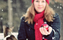a woman standing in the snow holding a Christmas ornament 