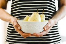 a woman holding a bowl of pears 