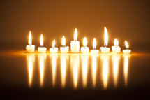 A line of burning votive candles and their reflection.