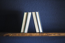 Four books on a wooden shelf against a blue wall.