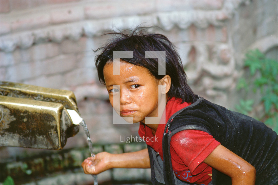 Nepalese girl child washing her hands and drinking from an outdoor spigot [For similar search ethnic smile]