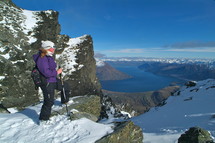 woman standing on top of snow capped mountain ridge overlooking river and mountains
