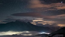 Panoramic view of Starry night sky with stars and colorful clouds in winter mountains with mist in valley time lapse
