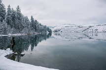 a woman with a backpack standing in front of a winter lake 