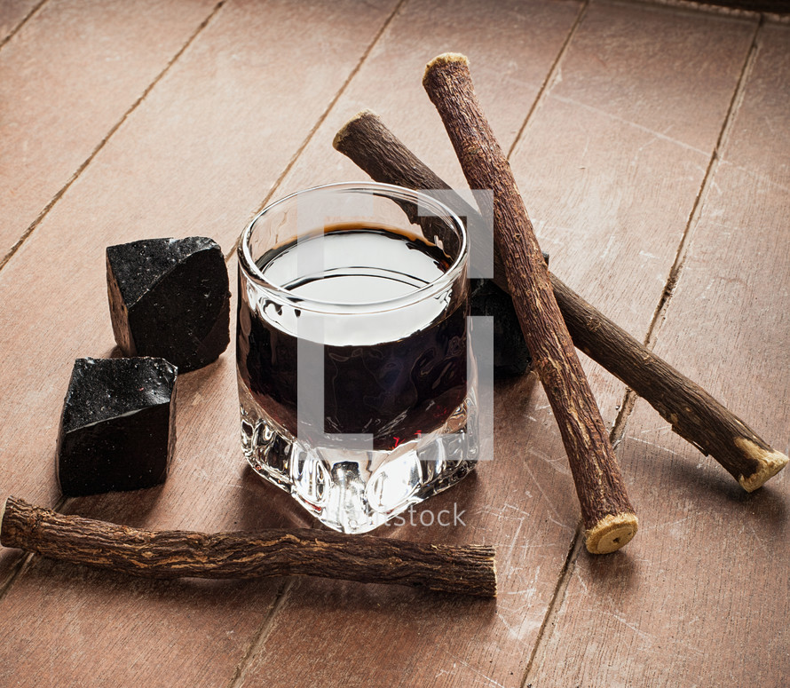 Licorice liqueur with pure blocks and roots on wooden table