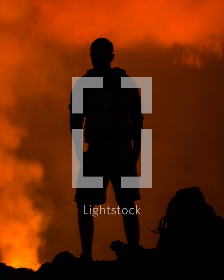 a silhouette of a man standing in front of a forest fire 