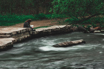 a woman sitting on rocks next to a fast flowing river 