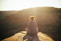 a woman sitting outdoors at the top of a canyon at sunset 