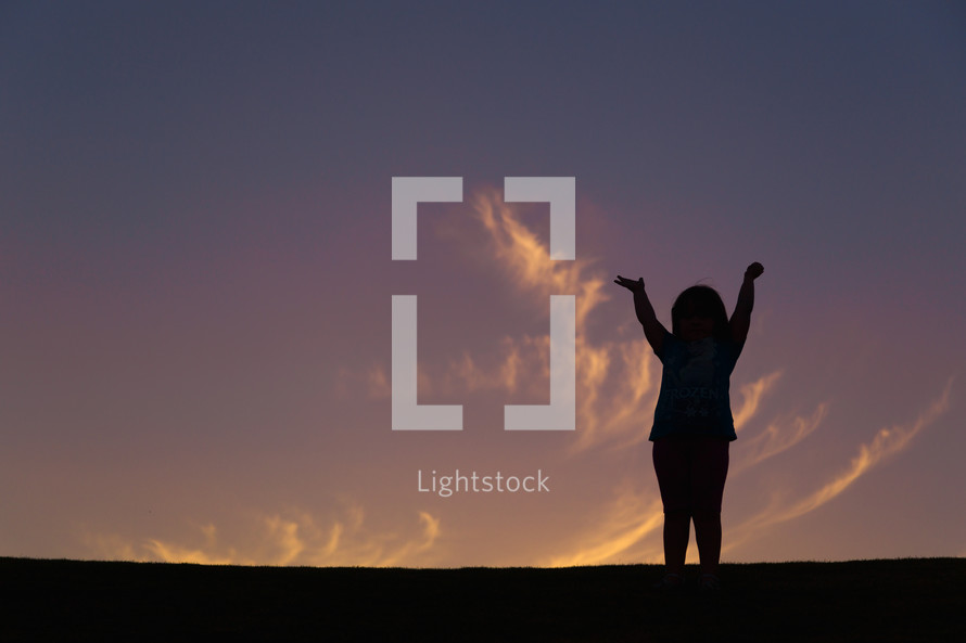 silhouette of a girl child with raised hands at sunset 