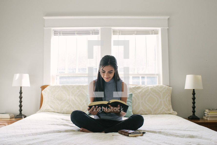A teen girl sitting on her bed and reading a Bible.